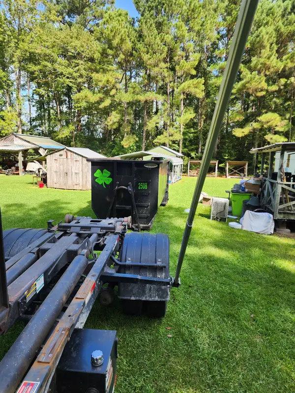 Irish Greens roll-off truck backing up to container 2508 on a lawn beside sheds